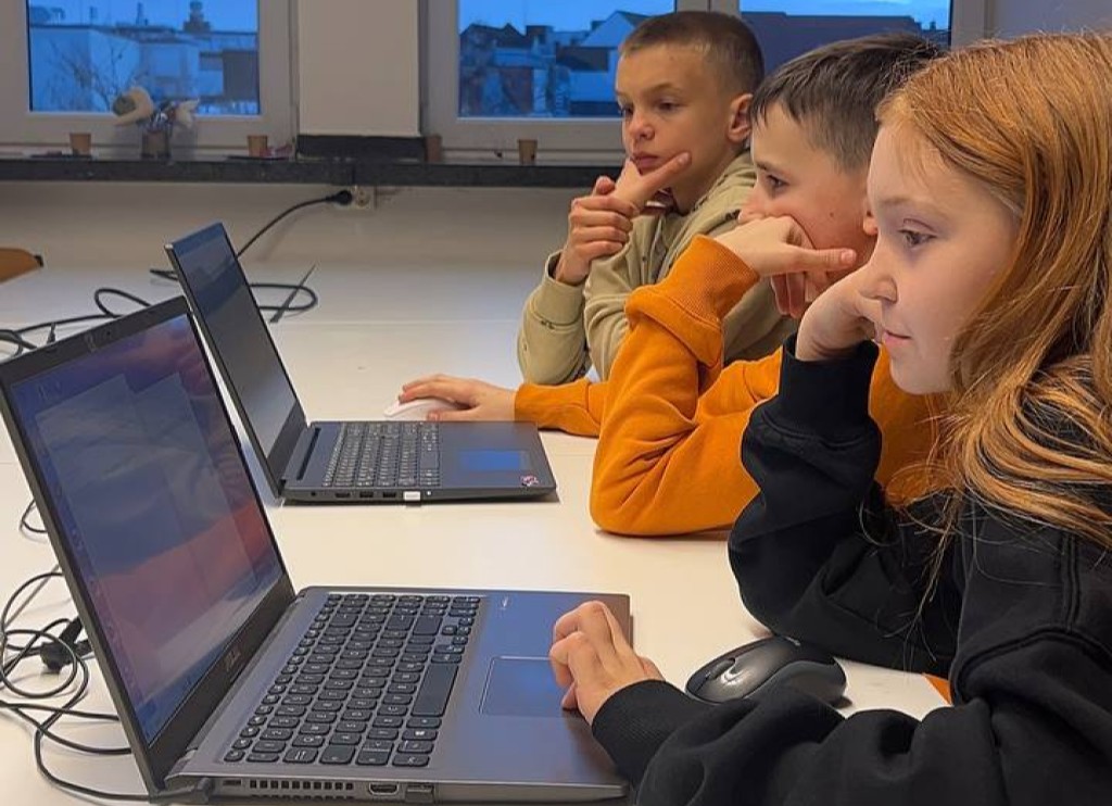Drei Kinder sitzen am Tisch mit Laptops und schauen konzentriert auf die Bildschirme