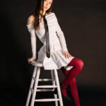 Ein Mädchen im weißen Kleid und roter Baskenmütze sitzt auf einem Hocker und posiert vor schwarzem Hintergrund.