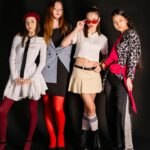 Vier Mädchen in auffälliger Modekleidung posieren gemeinsam vor schwarzem Hintergrund.