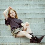 Mädchen sitzt lässig auf einer Steintreppe und blickt nach vorne.