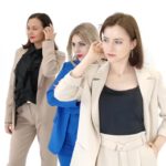 Drei Frauen in eleganten Anzügen posieren vor weißem Hintergrund.