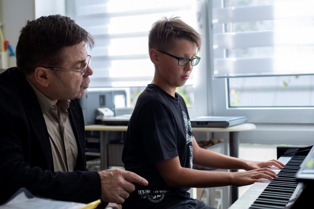Ein Musiklehrer erklärt einem Jungen am Klavier die richtige Handhaltung.