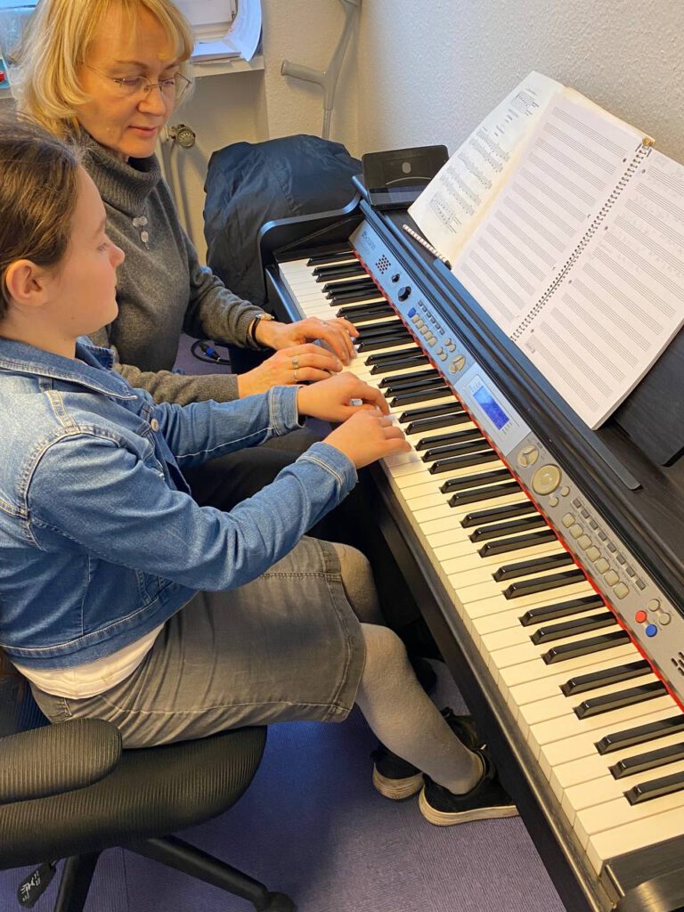 Eine Lehrerin spielt zusammen mit einem Mädchen am E-Piano und zeigt die Tastenfolge.
