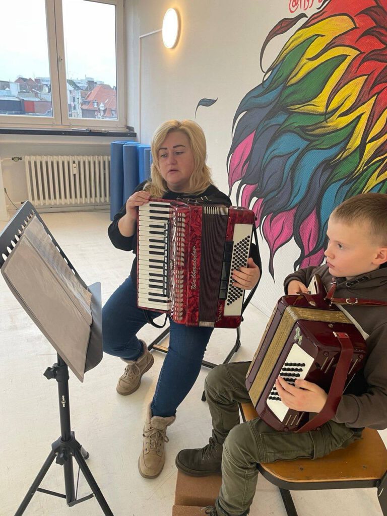 Eine Lehrerin und ein Junge spielen Akkordeon im Unterricht, beide halten Instrumente vor sich.