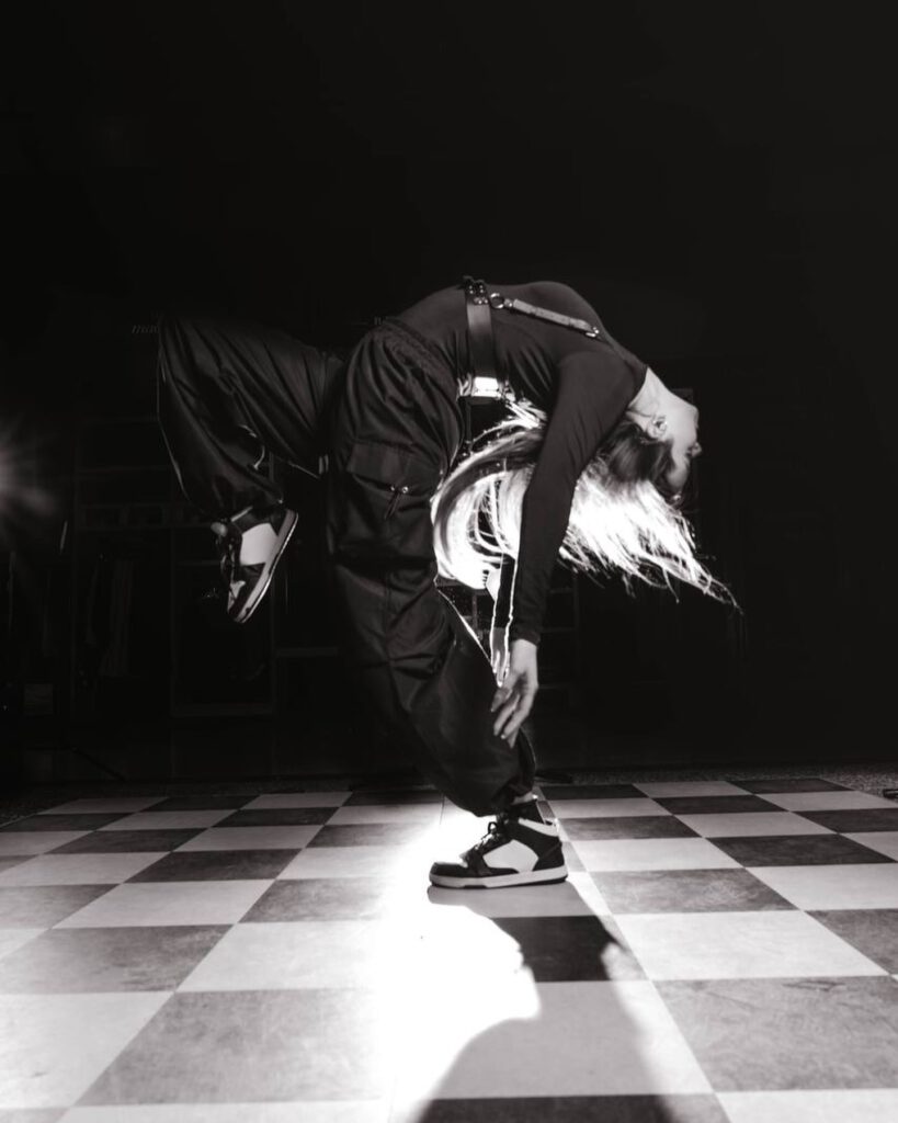 Tänzerin springt nach hinten in einer Akrobatikpose, Haare fliegen in der Luft.