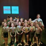 Группа девочек в костюмах гордо демонстрирует свои медали и кубки.