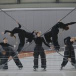 Группа детей в чёрной одежде выполняет творческую танцевальную позу у забора.