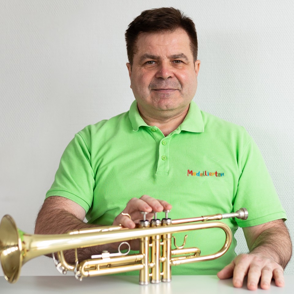 Ein Mann sitzt am Tisch und lächelt. Auf dem Tisch liegt ein Musikinstrument – eine Trompete.