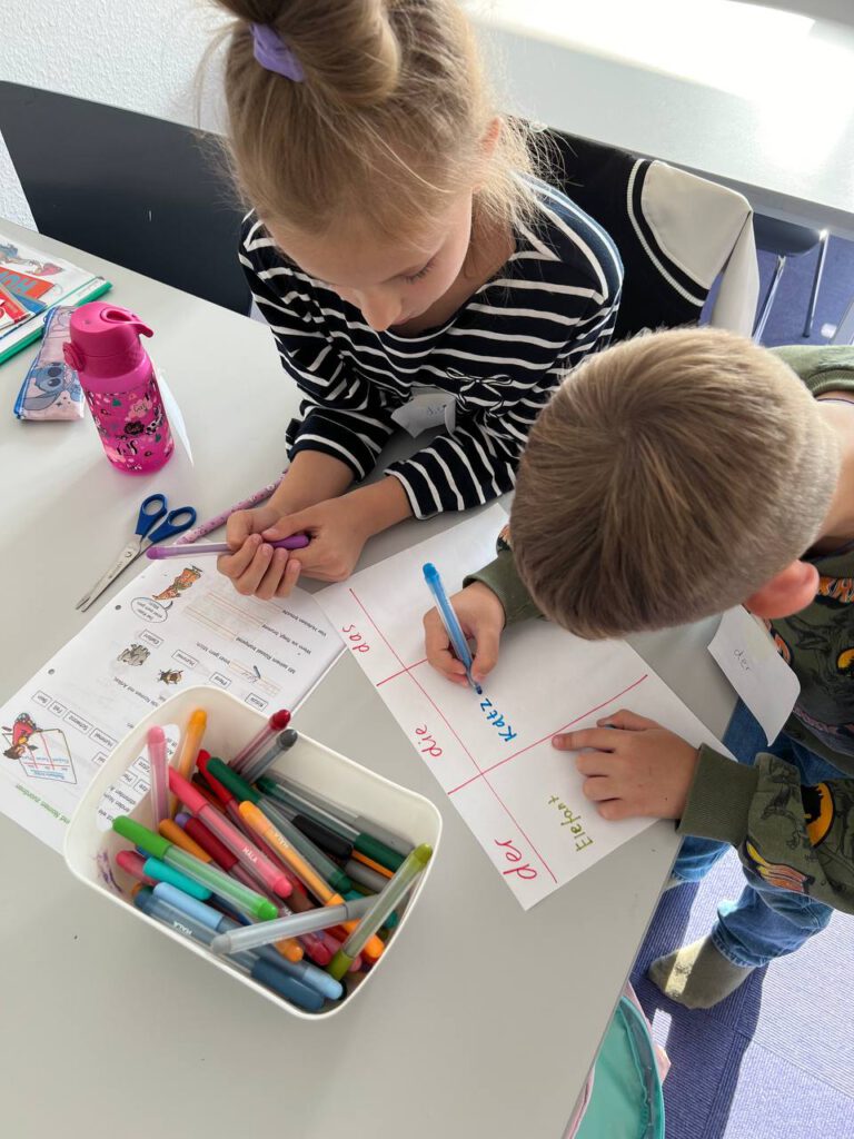 Zwei Grundschulkinder ordnen Wörter zu der/die/das an einem Tisch.