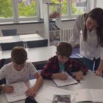 Учитель помогает двум ученикам выполнить задания в тетрадях.