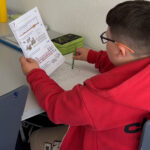 Ученик в красной толстовке выполняет упражнение по рабочему листу.