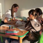 Учитель занимается с двумя девочками над рабочими листами в классе.