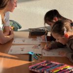 Учитель занимается с двумя девочками над рабочими листами в классе.