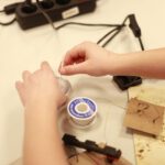 Крупный план: детские руки с припоем и инструментами на рабочем столе.