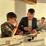 Наставник помогает ученику паять небольшую плату.