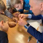 Преподаватель показывает детям деталь и объясняет эксперимент.