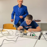 Преподаватель помогает мальчику при пайке на рабочем месте.