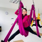 Teilnehmerin beim Aerial-Yoga: im pinken Tuch, Spagat-Pose, Studio.