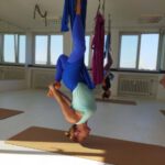 Tiefe Umkehrhaltung im blauen Tuch; Füße gefasst, ruhige Balance.