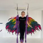 Mädchen steht im lila Tuch vor Wandflügeln – Moment des Schwebens.