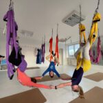 Drei Kinder hängen kopfüber in Tüchern und halten sich an den Händen.