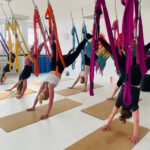 Erwachsenengruppe im herabschauenden Hund, Füße in Schlingen – Kräftigung.