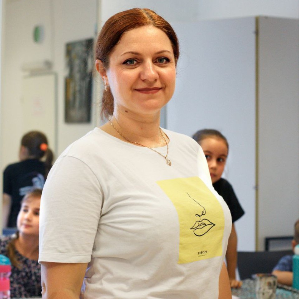 Die Frau lächelt, hinter ihrem Rücken schauen Kinder hervor.