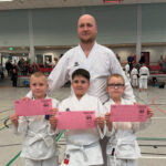 Тренер и трое детей показывают розовые карате-паспорта/сертификаты