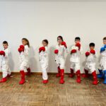 Дети в кимоно и защите, в ряд в боевой стойке у стены.