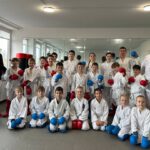 Большая группа каратэ с тренерами; участники позируют в перчатках.