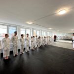 Zwei Reihen Schüler hören den Trainern im Dojo zu.
