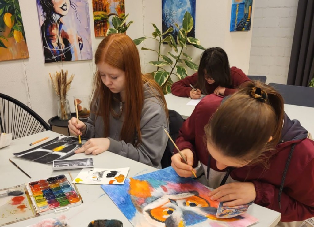 Mehrere Jugendliche sitzen am Tisch und malen mit Farben und Stiften auf Papier im Kunststudio.