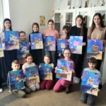 Kinder und Jugendliche posieren mit ihren fertigen Bildern von bunten Katzen und halten sie in den Händen.