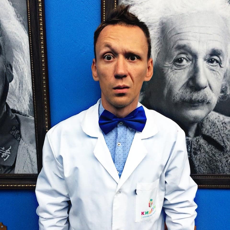 Ein Mann steht vor einem Porträt von Einstein und sieht überrascht aus.