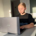 Schülerin schreibt am Laptop während des Programmierunterrichts; warmes Abendlicht.