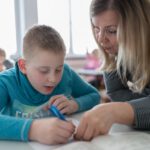 Педагог помогает ученику выполнить письменное упражнение по русскому языку.