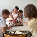 Trainer erklärt drei Kindern den nächsten Zug am Schachbrett.