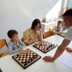 Kinder und Jugendliche spielen an zwei Brettern, Trainer unterstützt ruhig.