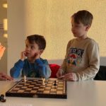 Zwei Kinder stehen am Brett mit Endspielstellung und verfolgen aufmerksam die Erklärung.