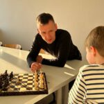 Trainer beugt sich über das Brett und erklärt dem Kind den nächsten Zug im Abendlicht.