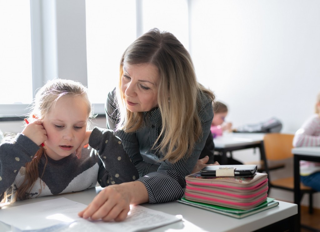 Lehrerin und Schülerin besprechen eine Aufgabe am Tisch, Fokus auf dem Text.