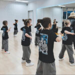 Группа детей танцует перед зеркалом под руководством педагога.