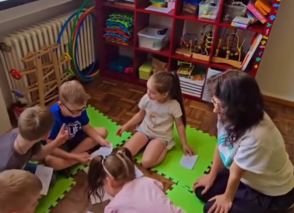 Kinder sitzen auf Matten und spielen ein Lernspiel im Sprachkurs.