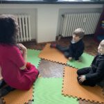 Игровая разминка: учитель и двое мальчиков беседуют, сидя на ковриках.