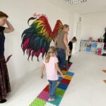 Дети и родители проходят босиком по тактильной дорожке; педагог сопровождает. На стене — яркие «крылья».