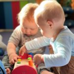 Двое малышей в солнечном свете играют с деревянной вставляющей игрушкой — тренируют мелкую моторику.