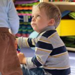 Мальчик сидит на полу и смотрит на другого ребёнка; на фоне — цветные коврики.