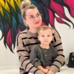 Мама держит ребёнка на коленях; на стене яркая роспись.