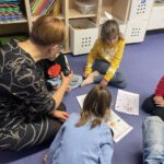 Урок русского для дошкольников: педагог с детьми на полу разбирают листы с заданиями и картинками.