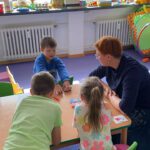 Парная работа и карточки: дети у окна обсуждают русские слова, педагог рядом.